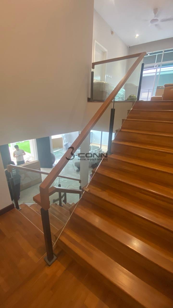 A tempered glass railing with a timber handrail beside timber treads, the glass held in slim posts.