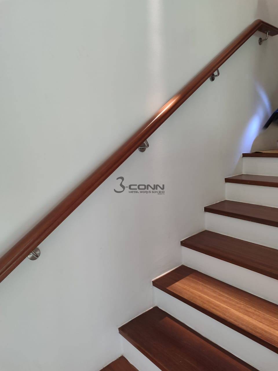 A Nyatoh timber handrail mounted on a white wall beside a flight of timber treads.